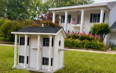 Columned house birdhouse on the lawn in front of the home it was made to match