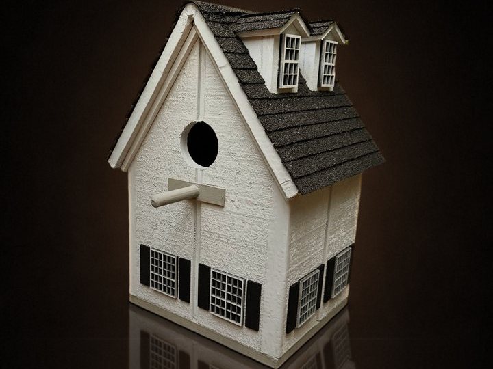 White cottage birdhouse with two dormers, black shutters and a shingle roof
